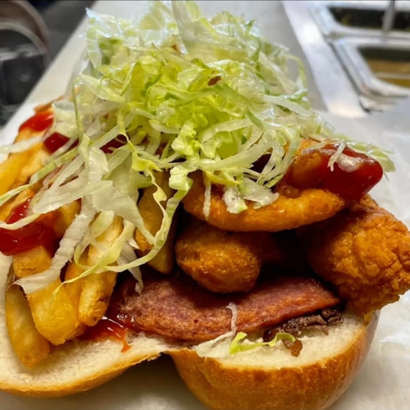 A Cedar Grill & Pizza sandwich overflowing with fries, chicken nuggets, pepperoni, lettuce, and ketchup.