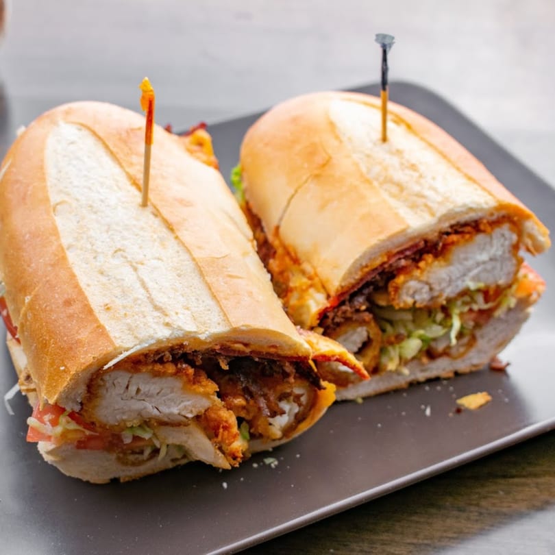 Two Italian chicken cutlet sandwiches with lettuce and tomato on a dark plate.