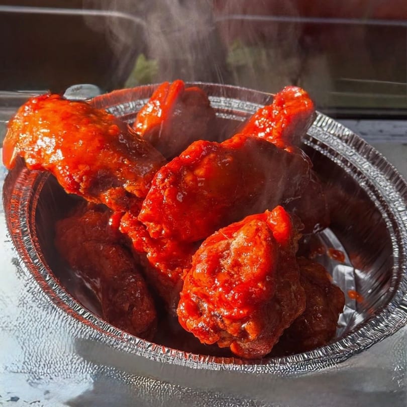 Steaming hot, bright red chicken wings in a silver foil container from Cedar Grill & Pizza.