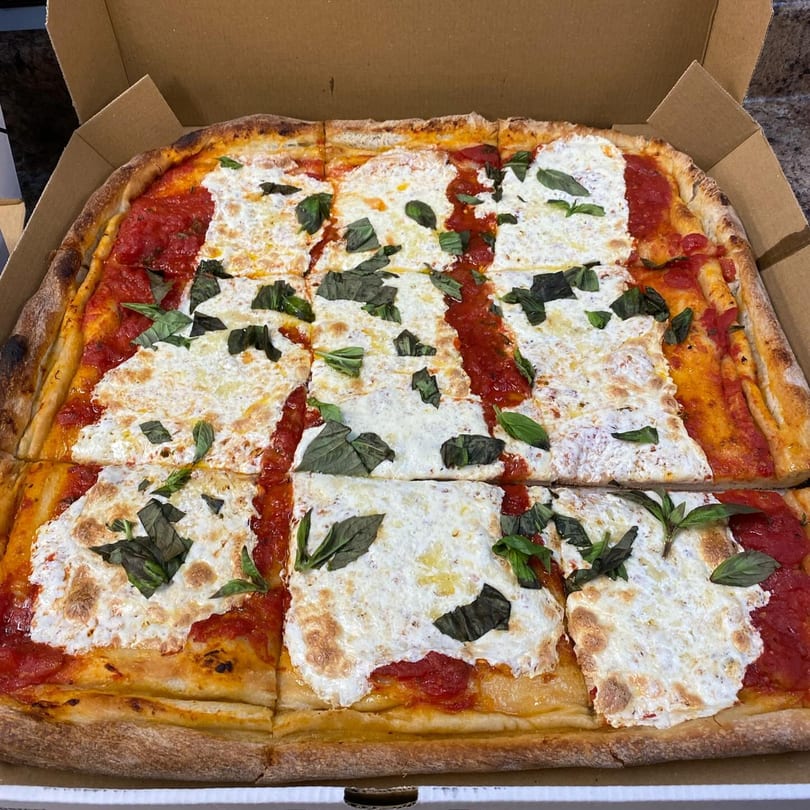 A rectangular Cedar Grill & Pizza Margherita pizza, cut into squares, with fresh basil in a delivery box.