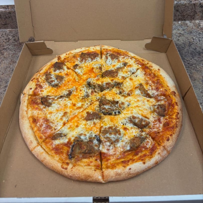 A whole, sliced Cedar Grill & Pizza Italian sausage pizza in a cardboard box.