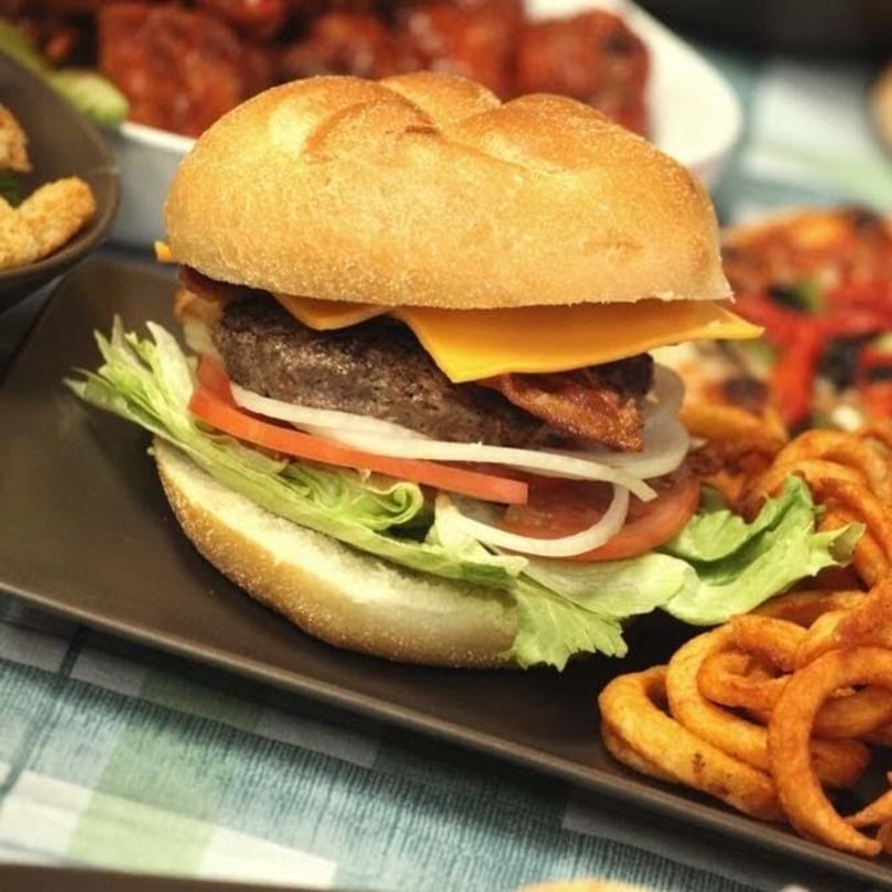 A beef burger with cheese, bacon, lettuce, tomato, and onion, served with curly fries.