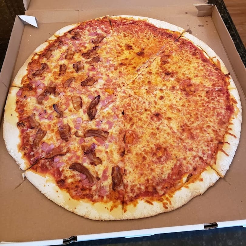 Half cheese, half meat pizza with ham and bacon in a Cedar Grill & Pizza box.